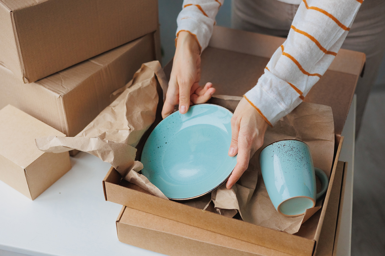woman packs handmade plates into boxes. small business and entrepreneurship. a business woman sends an order for delivery. online store selling tableware and home decor. kraft cardboard box